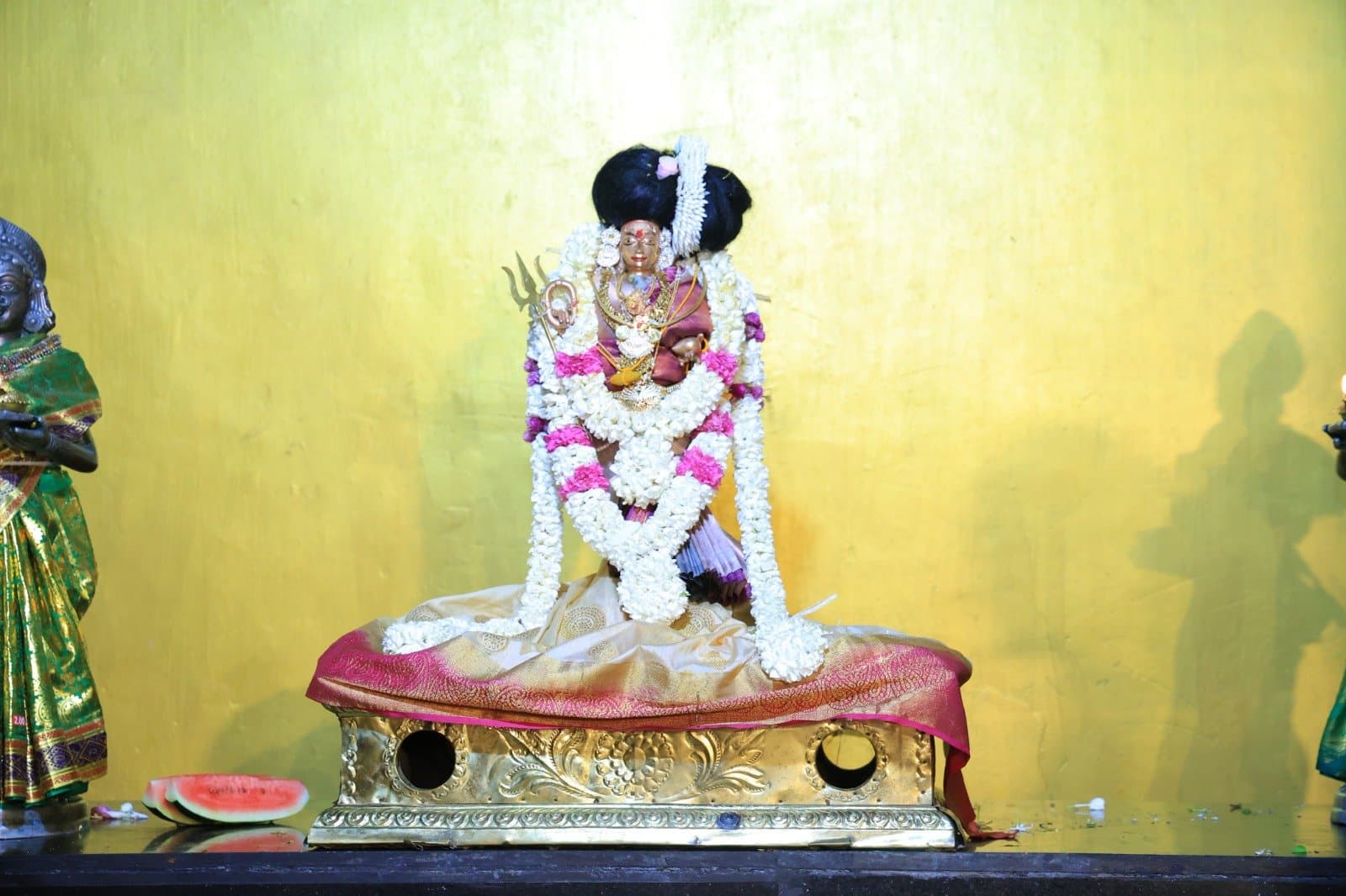 Smaller deity figure with trident and garlands on a golden seat