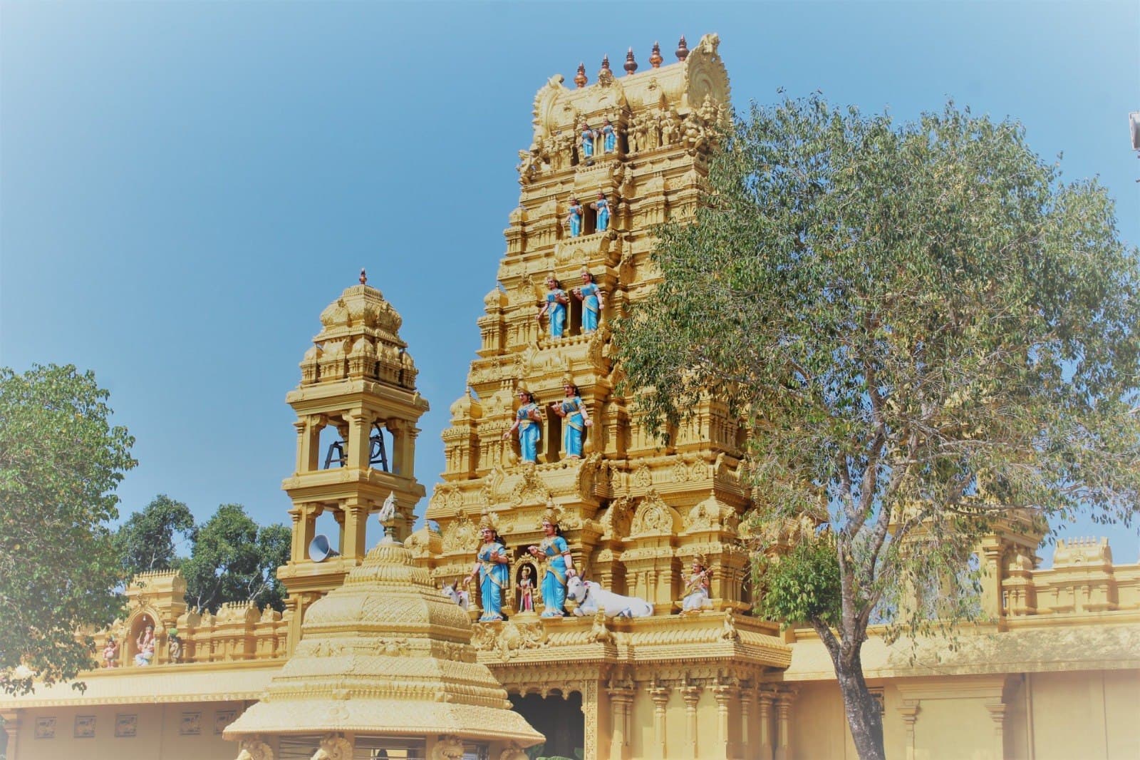 Golden gopuram and bell tower of Arasarpathi Kannagi Amman Potkovil under a clear blue sky